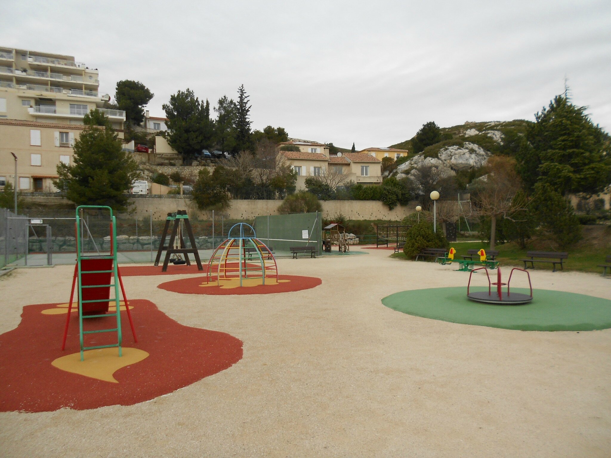  Terrain d' entraînement au tennis avec son mur, clôturé et jeux pour enfants à proximité.